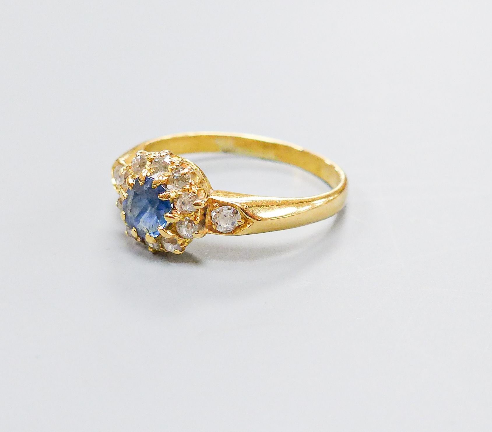 An 18ct, sapphire and diamond set circular cluster ring, with diamond set shoulders, size M, gross 3.4 grams.